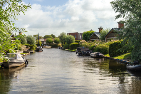 Scenic view of a canal lined with boats and cozy glamping accommodations surrounded by greenery.