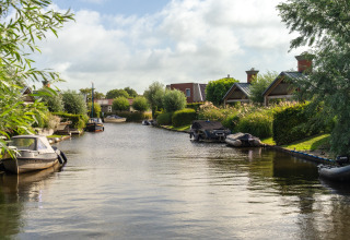 Idyllischer Blick auf einen Kanal mit Booten und luxuriösen Glamping-Unterkünften im Grünen.