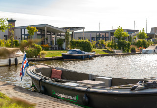 Foto van een moderne lodge aan het kanaal met kleine bootjes en groene tuinen op een zonnige dag.