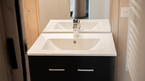 Lavabo moderno con specchio in bagno di un lodge, top bianco, mobile nero e pareti in legno chiaro.
