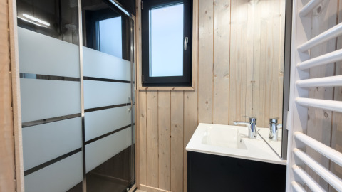 Baño moderno de lodge con paredes de madera clara, ducha con cristal esmerilado y ventana.