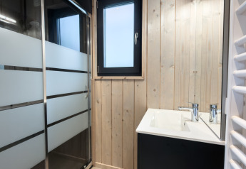 Moderne lodgebadkamer met lichte houten wanden, douche met matglas en een raam boven de wastafel.
