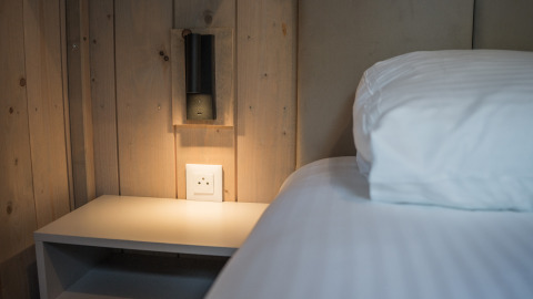 Modernes Schlafzimmer im Ecolodge, Hameau de la Semois, Belgien, mit Nachttisch, Lampe und weißer Bettwäsche.