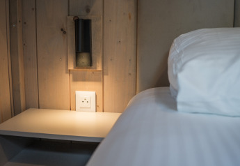 Moderne slaapkamer bij Ecolodge, Hameau de la Semois, België, met nachtkastje, lamp en wit beddengoed.