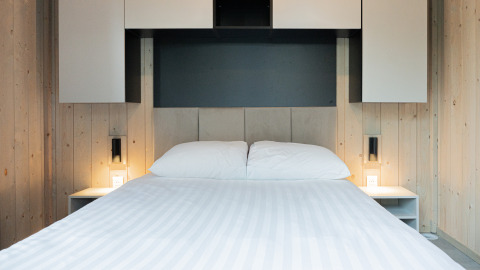 Moderne lodge-værelse med en nydelig seng, hvide puder, træpaneler og minimalistiske natborde med lys.