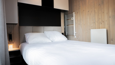 Camera di lodge moderna con letto matrimoniale, lenzuola bianche, pareti in legno e arredamento minimalista.