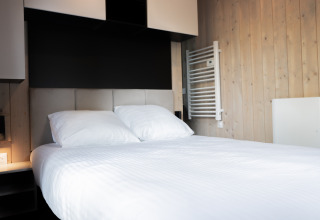 Habitación moderna de lodge con cama doble, sábanas blancas, paredes de madera y decoración minimalista.