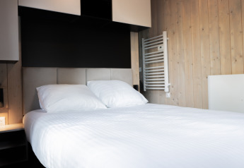 Modern lodge room with a double bed, white sheets, wooden panel walls, and minimalist decor.