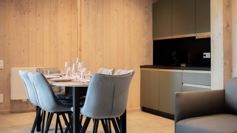 Modern dining area with six chairs and set table, next to a kitchenette in Ecolodge at Hameau de la Semois, Belgium.