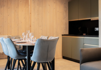 Moderner Essbereich mit sechs Stühlen und gedecktem Tisch neben Küche in der Ecolodge, Hameau de la Semois, Belgien.
