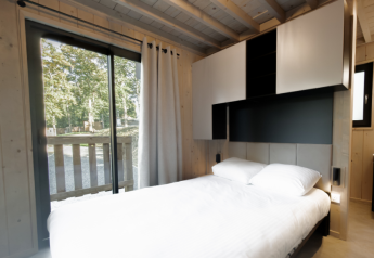 Modernes Schlafzimmer in einer Ecolodge mit Doppelbett, großen Schränken und Blick ins Grüne in Belgien.