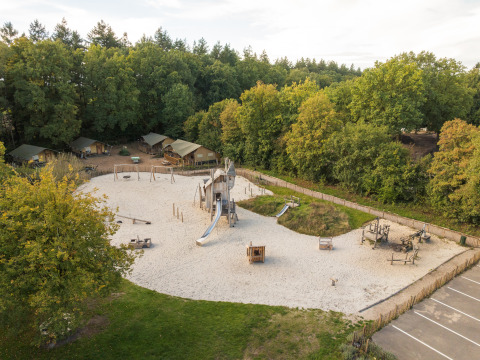 Spielplatz mit Rutschen und Safari-Zelten im Hintergrund, umgeben von Bäumen, aus der Vogelperspektive.