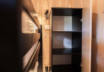 Interno della tiny house Ecolodge ad Hameau de l'Ourthe, Belgio, con letto a castello e armadio aperto.