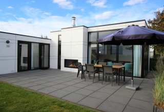 Lodge moderne L-Cube 6 à Schoneveld, Pays-Bas, terrasse avec cheminée extérieure et parasol visible.