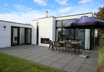 Moderne L-Cube 6 lodge in Schoneveld, Nederland met terras, open haard, tafel en groot parasol.