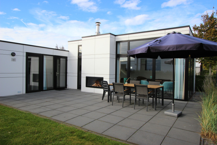 Lodge L-Cube 6 en Schoneveld, Países Bajos, con terraza, chimenea, mesa y sombrilla exterior moderna.