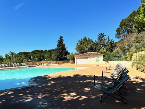 Piscina al aire libre en Camping d'Aix en Provence rodeada de tumbonas, árboles y cielo azul claro.