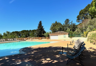 Piscina all'aperto al Camping d'Aix en Provence con lettini, alberi e un cielo azzurro splendente.