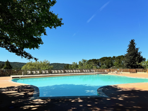 Vista de la piscina en Camping d'Aix en Provence, rodeada de tumbonas y colinas arboladas en Francia.