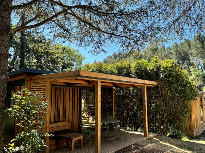 Vista exterior del Victoria Chalet, una cabaña de madera con terraza rodeada de árboles y arbustos verdes.