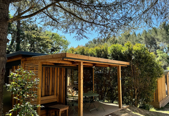 Vista exterior del Victoria Chalet, una cabaña de madera con terraza rodeada de árboles y arbustos verdes.