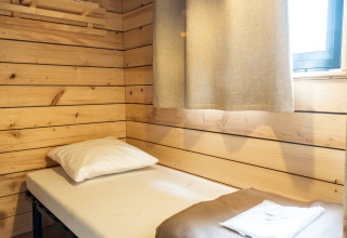 Simple wooden cabin room with a single bed, pillow, blanket, and window in Evasion Chalet, Aix en Provence.