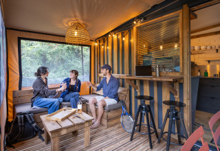 Tres amigos conversan y beben en el interior de la cabaña Arizona en Camping d'Aix en Provence, Francia.