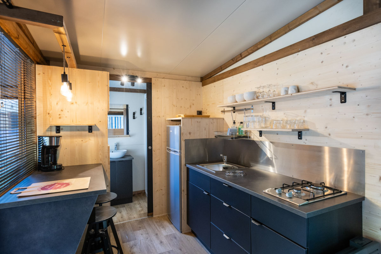 Moderne houten keuken met zwarte aanrecht, open planken, gaskookplaat en kleine eethoek in een hut.