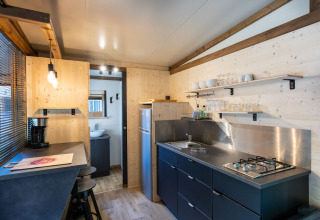 Cocina moderna de cabaña de madera con encimeras, estantes abiertos, estufa de gas y zona de comedor.