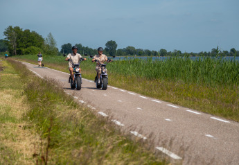 Twee mensen rijden met elektrische scooters op een fietspad aan het meer bij Vakantiechalet comfort+ in Nederland.