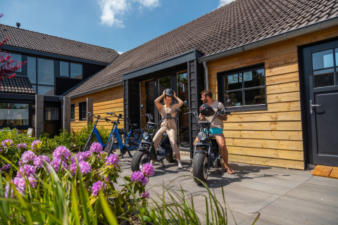 Due persone si preparano per un giro in bici fuori da uno chalet in legno al Vakantiepark De Wiedense Meren nei Paesi Bassi.
