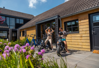 Due persone si preparano per un giro in bici fuori da uno chalet in legno al Vakantiepark De Wiedense Meren nei Paesi Bassi.