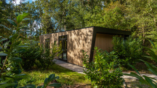 Modern tiny house Bosrand Wellness Cabin Premium surrounded by greenery, with wood siding and large windows.