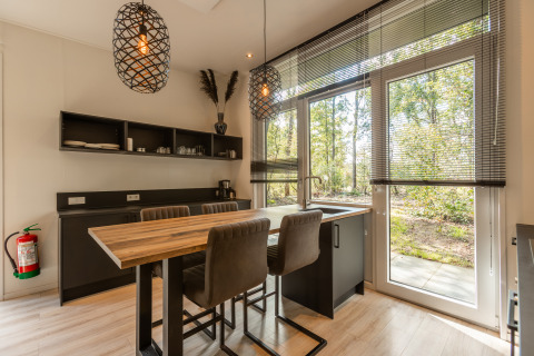 Modern cozy kitchen and dining area in a tiny house with large windows overlooking nature in the Netherlands.