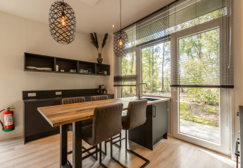 Modern cozy kitchen and dining area in a tiny house with large windows overlooking nature in the Netherlands.