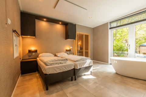 Modern slaapkamerinterieur van Bosrand Wellness Cabin Premium met vrijstaand bad en uitzicht op bos.
