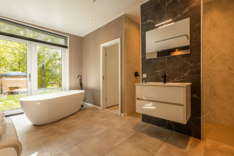 Moderne badkamer met vrijstaand bad, grote spiegel en tuinzicht in Bosrand Wellness Cabin Premium.