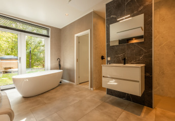 Modern bathroom with freestanding bathtub, large mirror, and garden view in Bosrand Wellness Cabin Premium.