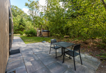 Terrazza esterna della Bosrand Wellness Cabin Premium con tavolo, sedie e vasca idromassaggio nei Paesi Bassi.