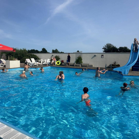 Families and children enjoy a sunny day swimming and playing at Hvalpsund Familie Camping pool in Denmark.