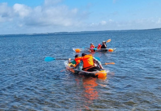 Personas en kayak en un lago cerca de Farsø, Dinamarca, con chalecos salvavidas bajo un cielo azul.