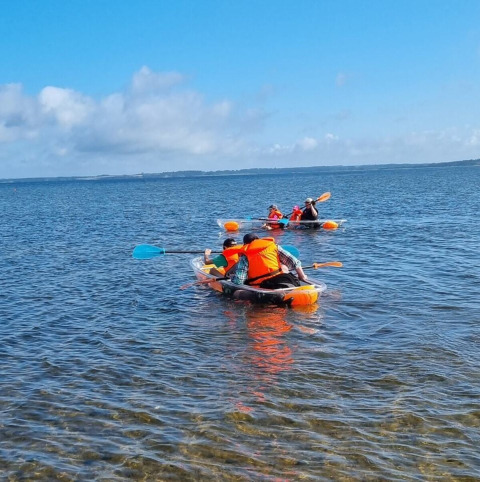 People kayaking on a lake near Farsø, Denmark, wearing life jackets under a clear blue sky.