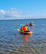 Personas en kayak en un lago cerca de Farsø, Dinamarca, con chalecos salvavidas bajo un cielo azul.