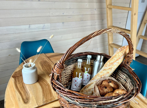 Kurv med baguette, croissanter og drikke på træbord i hyggelig hytte ved Domaine des Feuilles, Frankrig.