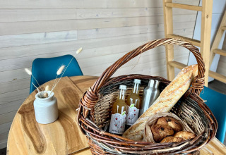 Picknickkorb mit Baguette, Croissants und Getränken auf Holztisch in Domaine des Feuilles, Frankreich.