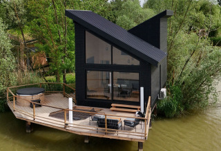 Cabina moderna nera con tetto inclinato e terrazza sull’acqua al Domaine des Feuilles, Auvergne-Rhône-Alpes, Francia.