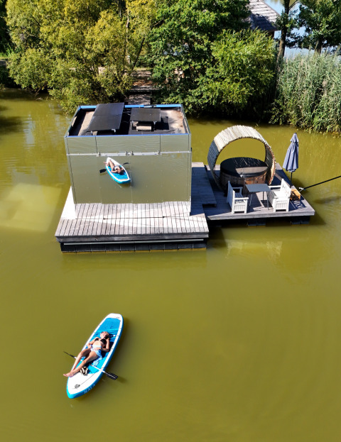 Luchtfoto van een drijvende hut met terras en persoon op paddleboard bij Domaine des Feuilles, Frankrijk.