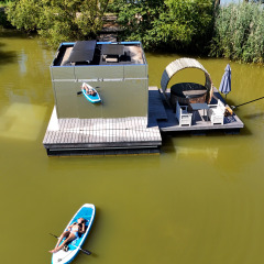 Luchtfoto van een drijvende hut met terras en persoon op paddleboard bij Domaine des Feuilles, Frankrijk.