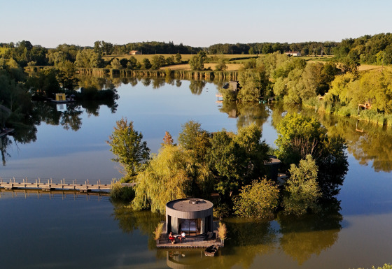 Vista aérea de una cabaña junto al lago rodeada de árboles en Domaine des Feuilles, Auvergne-Rhône-Alpes, Francia.