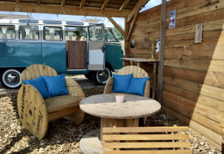 Udendørs siddeområde med genbrugsmøbler ved siden af en klassisk VW van i Domaine des Feuilles, Frankrig.